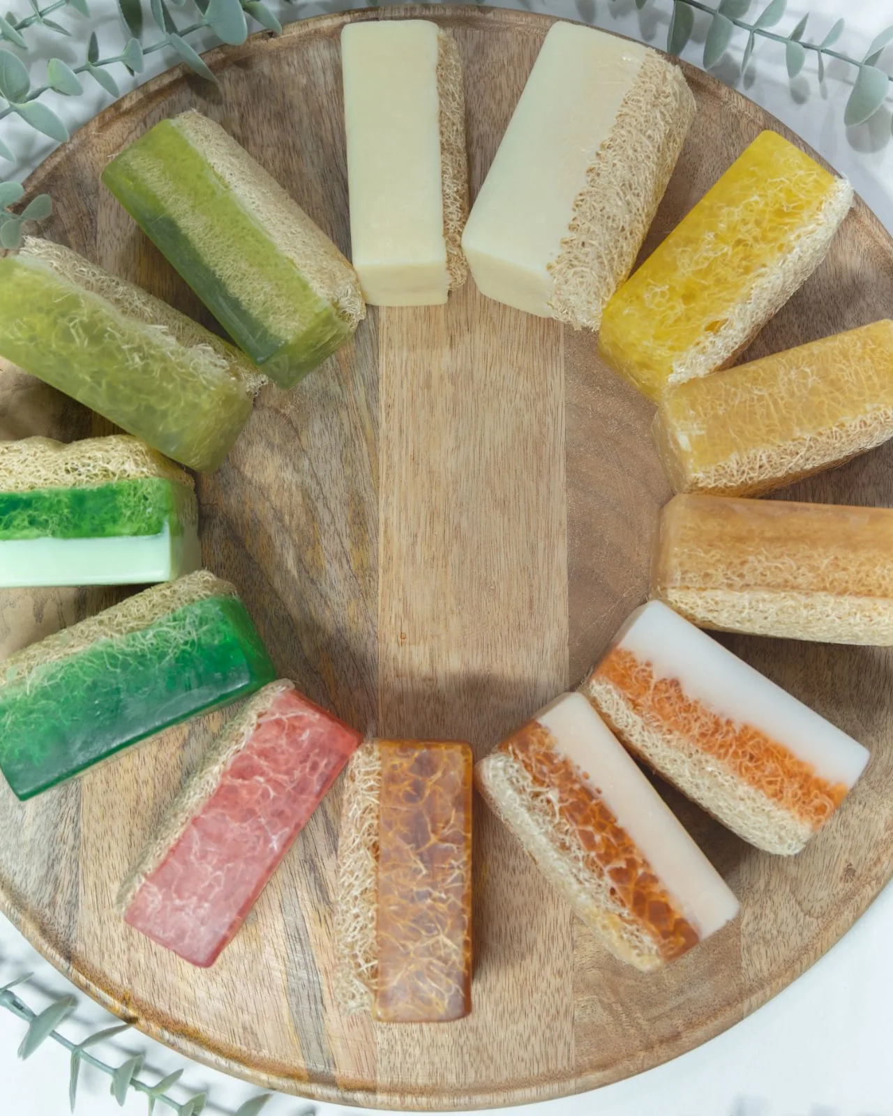 Les savons One Touch Éclat disposés en cercle sur un plateau de bois, du crème au vert, au rose et à l'ambre